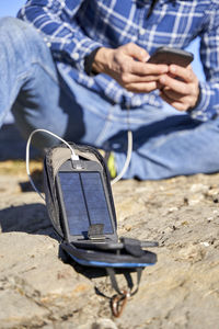 Man charging mobile phone through portable solar panel on sunny day