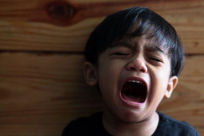 Close-up of boy crying against wood