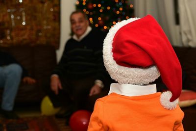 Rear view of boy wearing santa hat standing at home during christmas