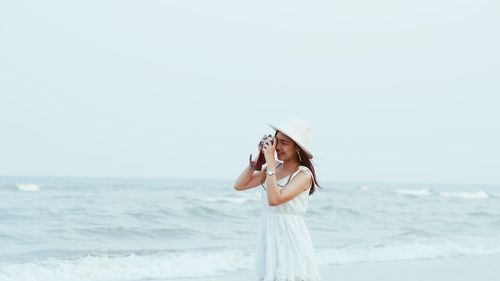 Woman photographing by sea against clear sky