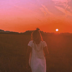 Rear view of woman with umbrella on field against sky during sunset