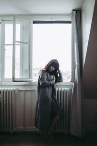 Young woman standing against window at home