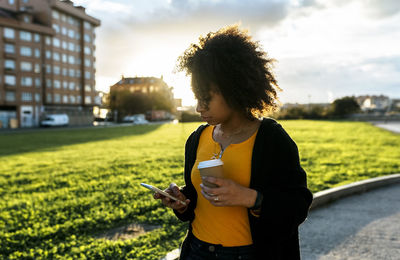 Young woman using mobile phone while standing on field