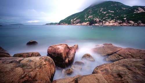 Scenic view of sea against mountain seen from rocky shore at shek o