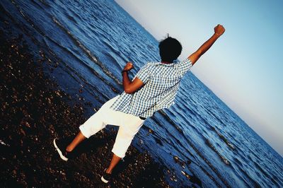 Rear view of woman sitting on wood against sea