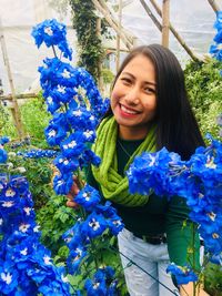 Portrait of smiling young woman standing by flowering plants