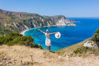 Happy woman raising hands with feeling of freedom, petani beach. cephalonia island, greece