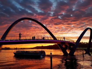 Bridge over river in city at sunset