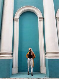 Full length of young woman standing against blue building