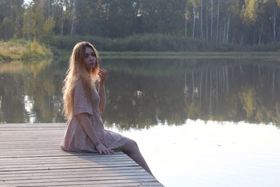 Portrait of woman sitting on pier over lake