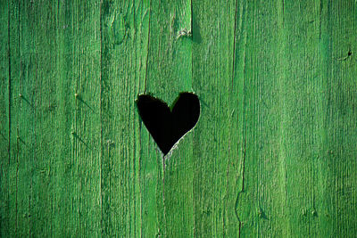 Heart shaped hole in a green wooden door