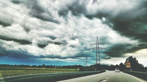 Road passing through field against cloudy sky