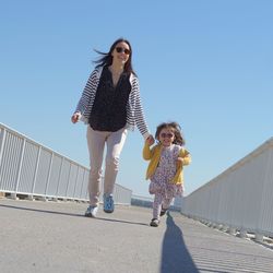 Happy girl walking on walkway against clear sky