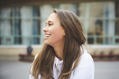 Smiling teenage girl looking away while sitting in schoolyard