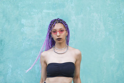 Portrait of woman with blue braided hair standing against wall