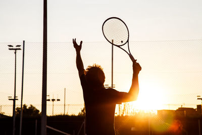 Rear view of silhouette young man playing tennis at court