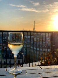 Wine glass on table by sea against sky during sunset