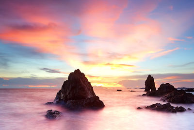 Rock formation in sea against romantic sky at sunset