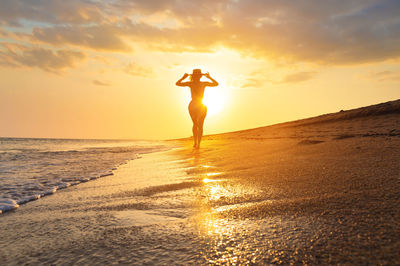 Rear view of man standing at beach against sky during sunset