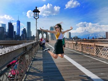 Full length of woman walking on bridge in city against sky