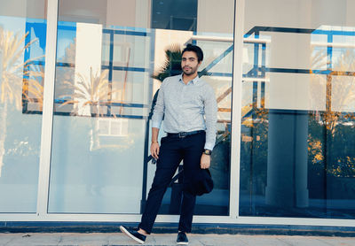 Full length portrait of young man standing against glass 