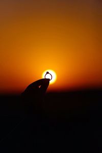 Cropped image of silhouette hand holding ring against sun during sunset