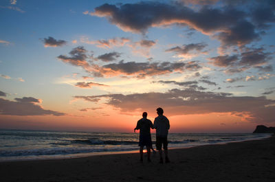 Silhouette friends standing on beach against sky during sunset