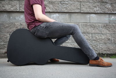 Low section of man sitting on guitar case against wall