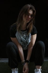 Portrait of young woman standing against black background