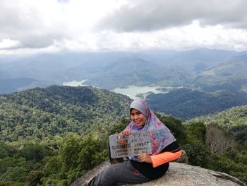 Portrait of smiling woman wearing hijab sitting on mountain against sky