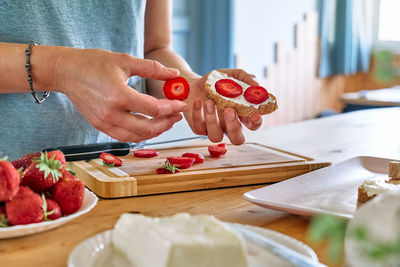 Female hands putting slices of ripe red strawberry on toast with spread stracchino cheese.