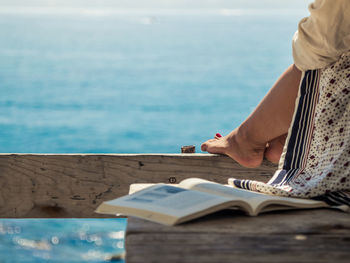 Low section of woman on book by sea