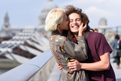 Girlfriend kissing cheerful boyfriend in city