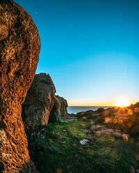 Rock formations in sea against clear sky during sunset