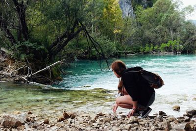 Woman crouching at riverbank in national park