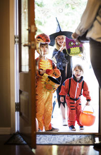 Cheerful siblings dressed for halloween party standing at door