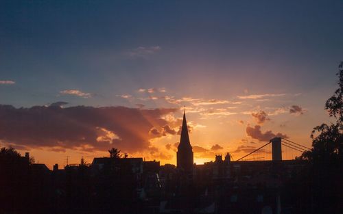 Silhouette of city against cloudy sky during sunset