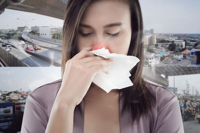 Digital composite image of woman wiping nose against cityscape