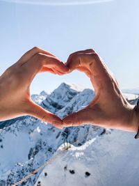 Cropped image of hand making heart shape against sky during winter