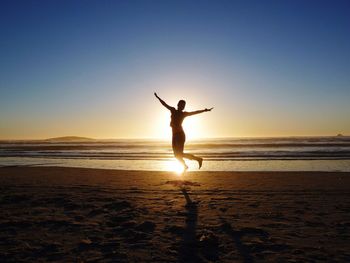 Full length of silhouette woman jumping at beach against clear sky during sunset