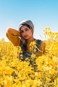 Portrait of young woman with arms raised on field against clear sky