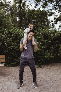 Cheerful father carrying son on shoulder in playground