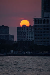 Silhouette buildings by sea against sky during sunset