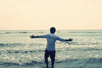 Rear view of silhouette man standing on beach against clear sky