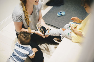 Mother with toddler dressing son's shoes at home