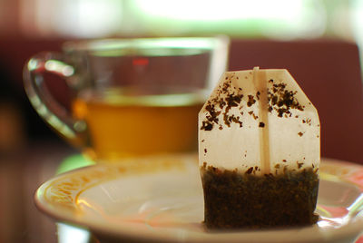 Close-up of tea bag in plate by cup on table