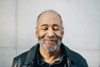 Smiling senior man with eyes closed against wall