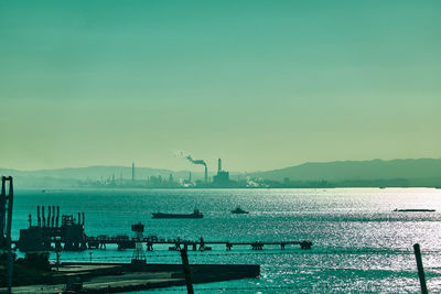 Scenic view of sea and factory against clear sky during sunrise