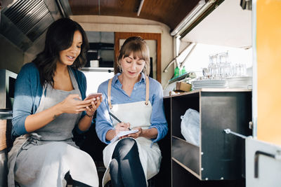 Female owner using smart phone while sitting with coworker in commercial land vehicle