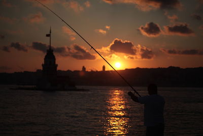 Silhouette man fishing in sea against sky during sunset